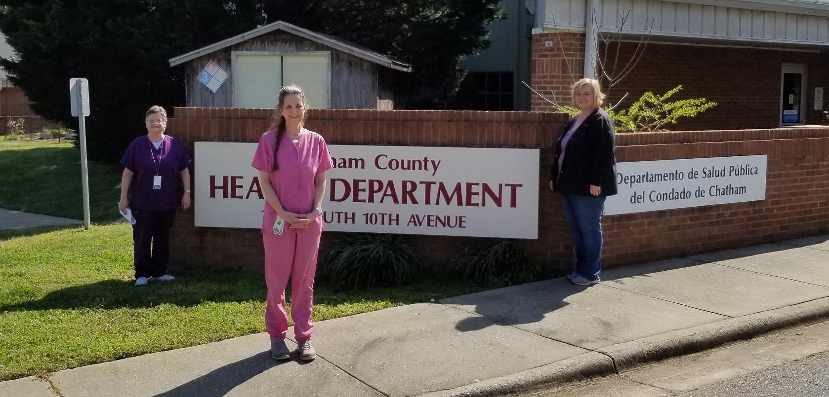 Three women in nurse scrubs stand in front of a sign that reads Chatham County Public Health Department