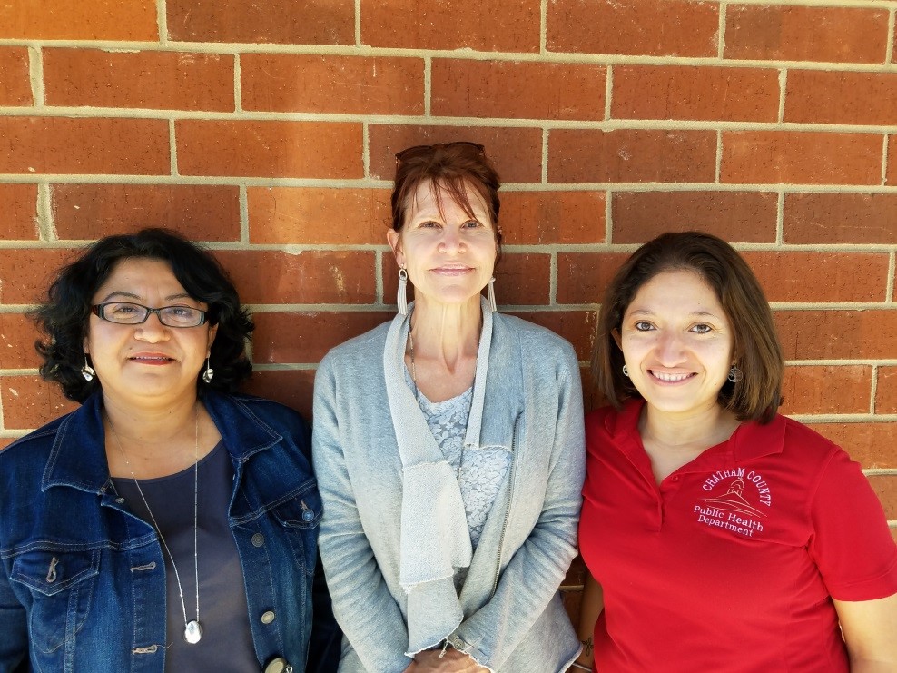 Three women standing against a brick wall