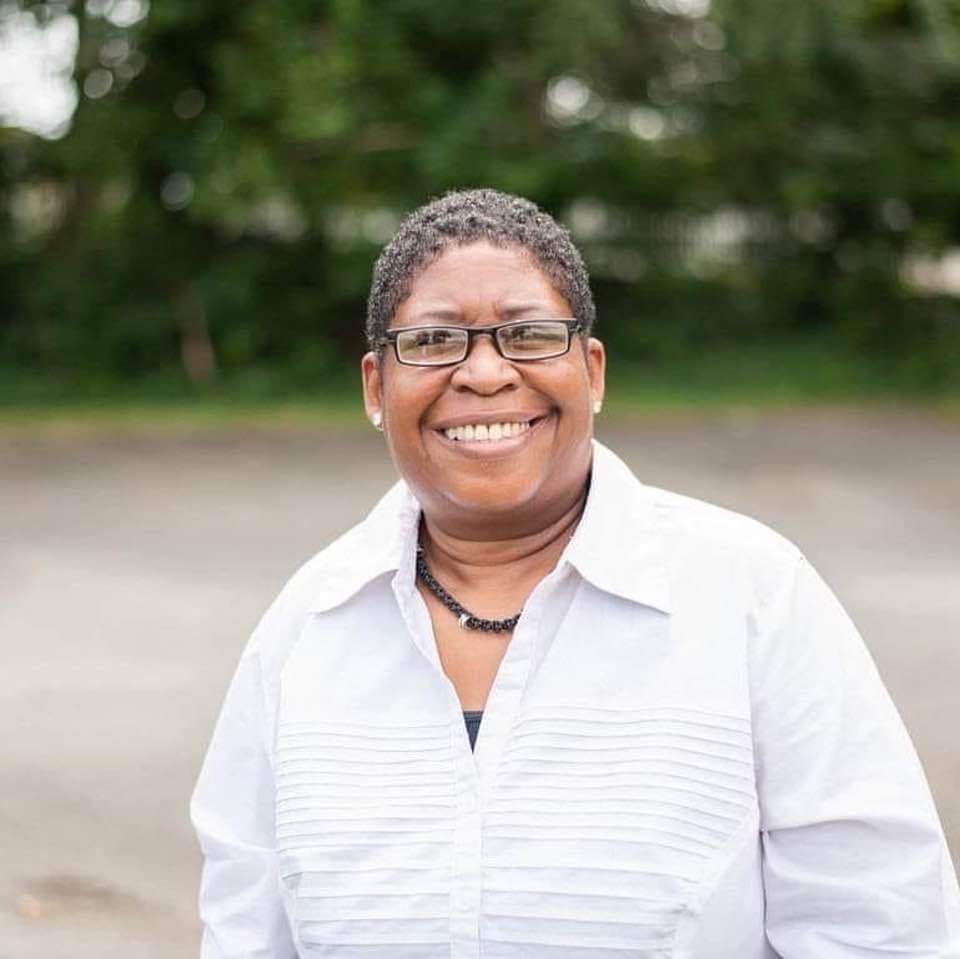 A Black woman looking at the camera and smiling while standing outside.