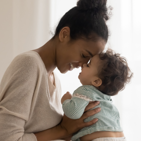 A young mother holds her child in a room with a white curtain in the background.