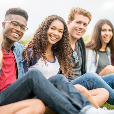 Four teenagers, including two males and two females, smile while sitting on grassy hill and looking at the camera.