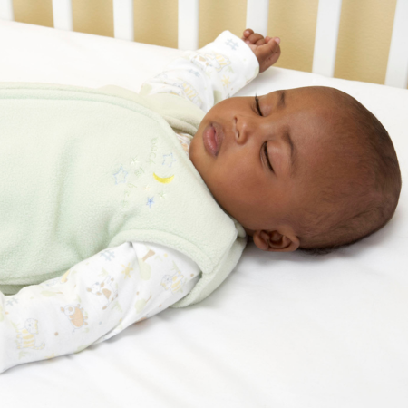 A baby lies on their back in a sleep sack.